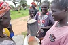 Women in South Sudan smile as they fill canisters with sorghum. csi